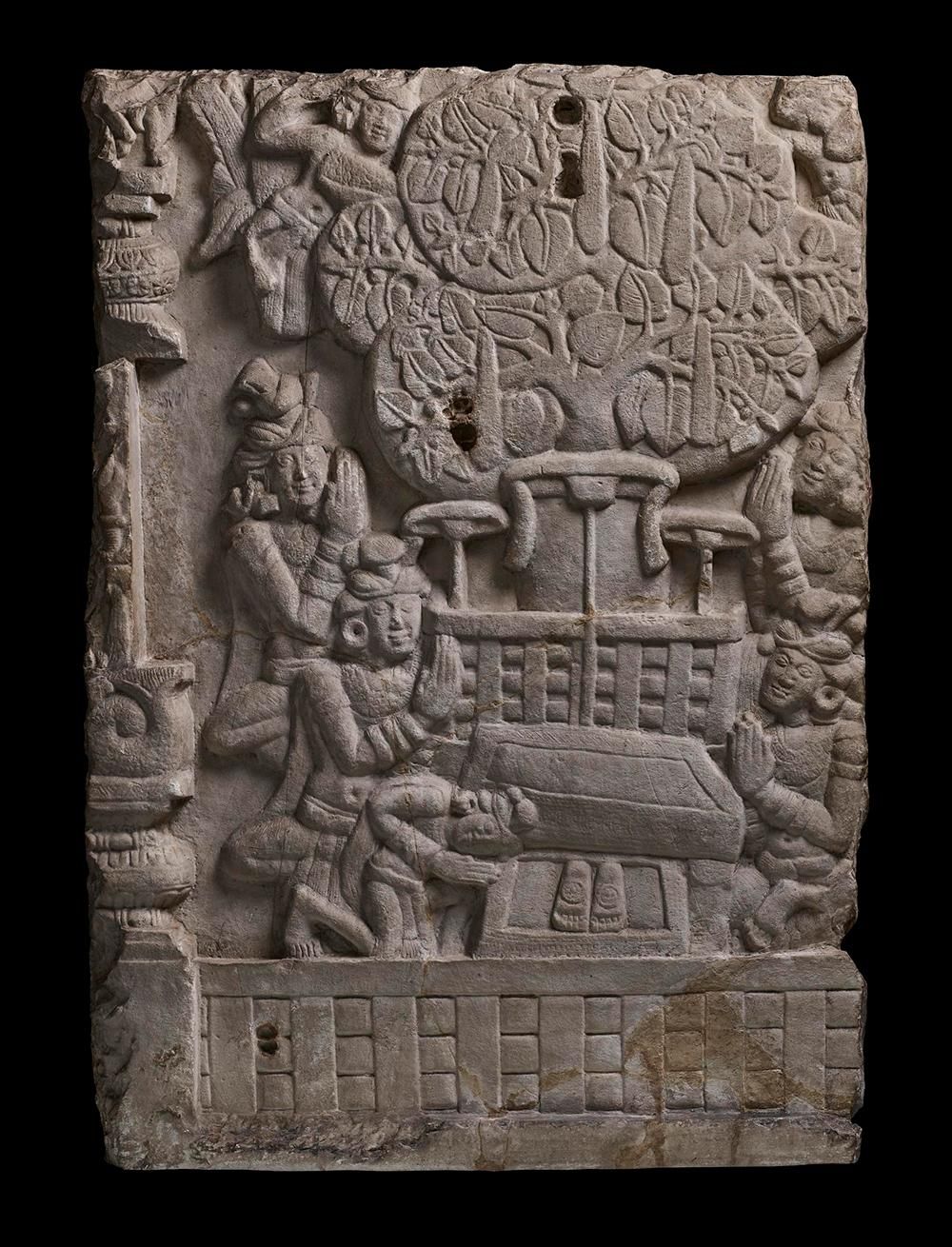 Rectangular limestone carving of a tree with an empty throne below it, flanked by four figures.