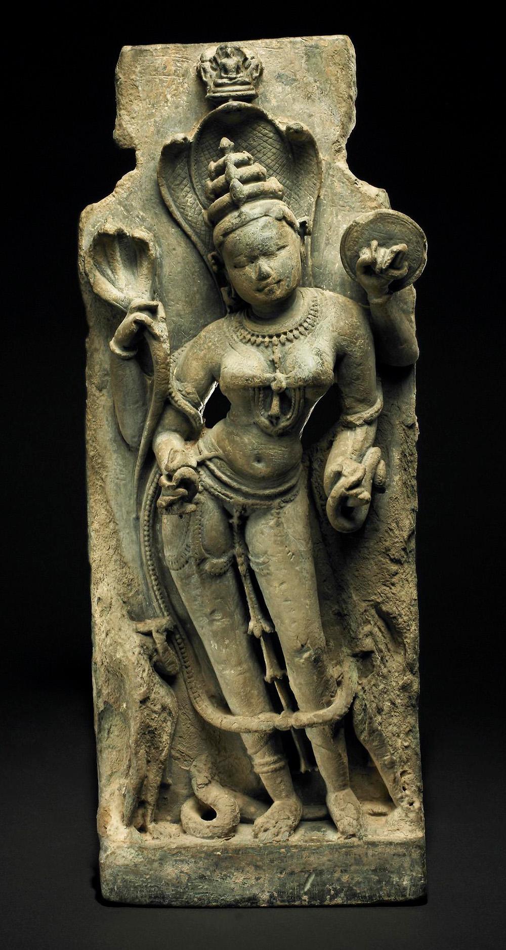 A carved sandstone figure of the goddess Padmavati wearing a headdress and snake canopy and holding a snake.