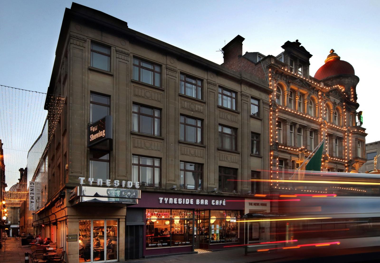 View of the Tyneside Cinema, a four-floor building on a street corner with outdoor seating.