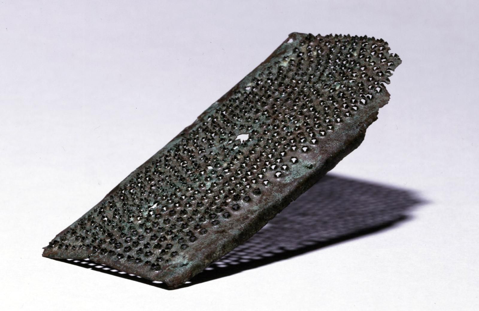 Rectangular sheet of bronze dotted with spiky ridges for grating similar to what we would use today, eroded